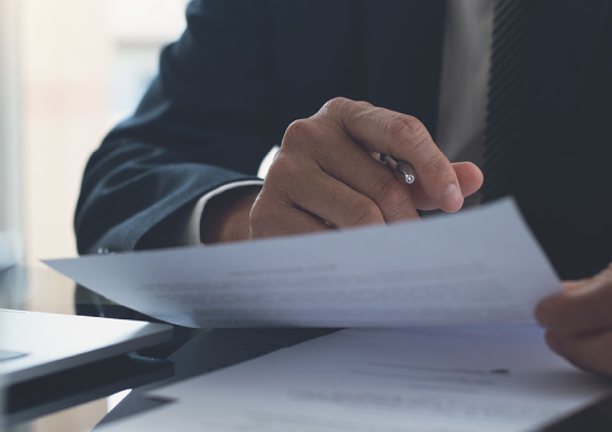close up of office worker inspecting copywriting paper document with a pen in hand